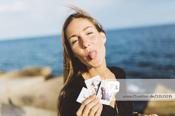 Cheeky young woman showing instant photos of herself at the seafront