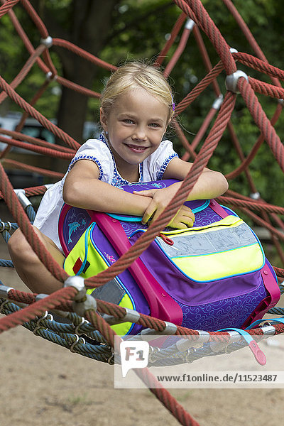 Porträt eines lächelnden Mädchens mit Schultasche im Nest sitzend auf dem Spielplatz