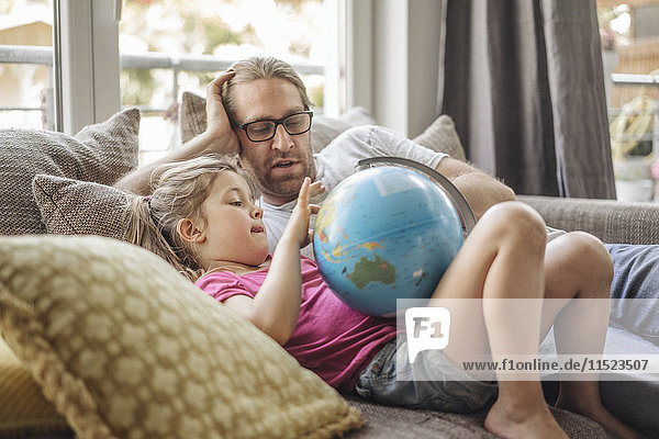 Vater und Tochter liegen mit Globus auf Sofa
