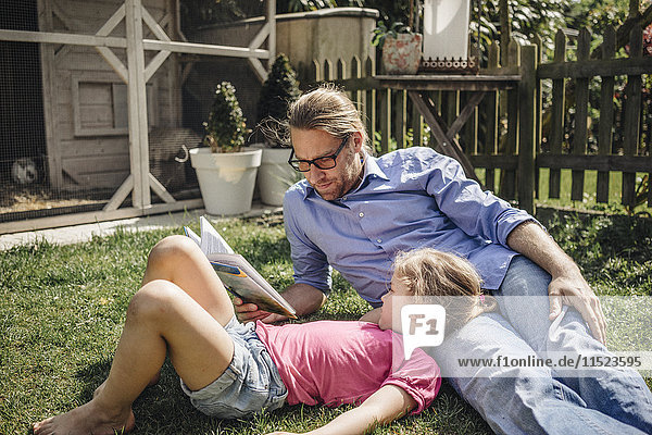 Father reading book with daughter in garden