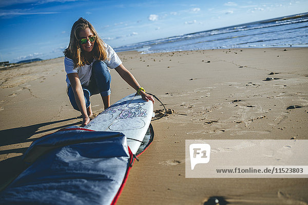 Junge Frau  die das Surfbrett aus der Abdeckung am Strand nimmt