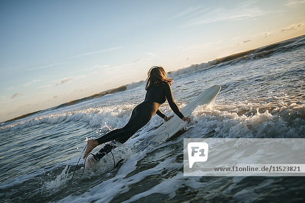 Surfer woman dressed in wetsuit entering the sea with surfboard