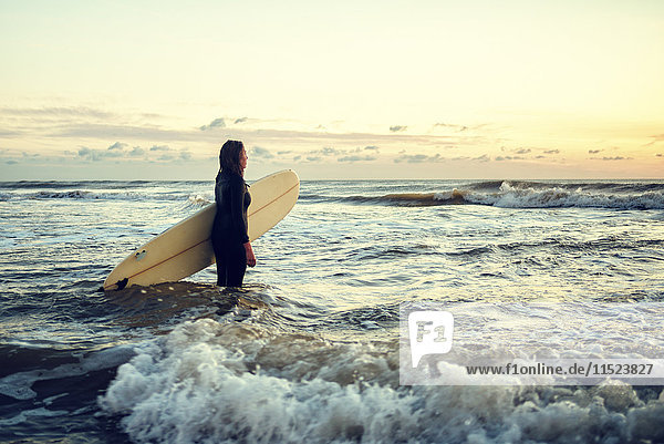 Junge Frau mit Surfbrett bei Sonnenuntergang