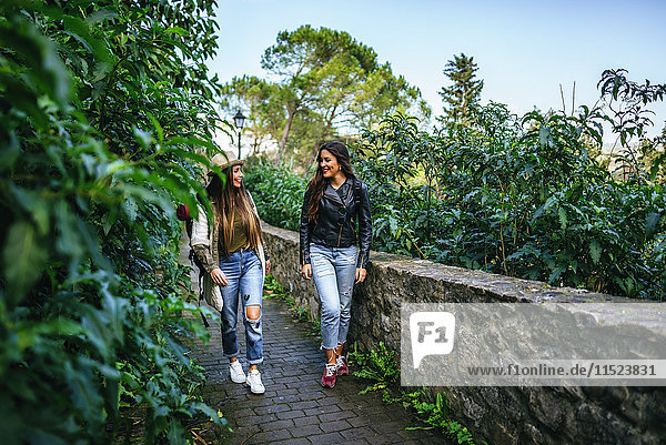 Zwei lächelnde junge Frauen  die auf einem Weg mit Pflanzen gehen.
