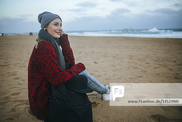 Smiling young woman sitting on the beach in winter