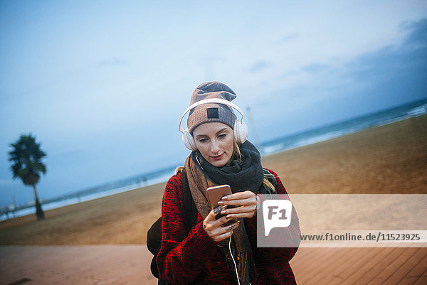 Young woman listening to music on a smartphone on the beach at dusk