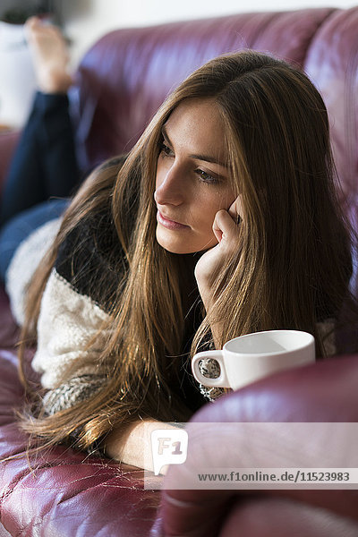 Junge Frau auf der Couch liegend mit Tasse Kaffee