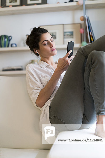 Woman on couch listening music with earphones and smartphone