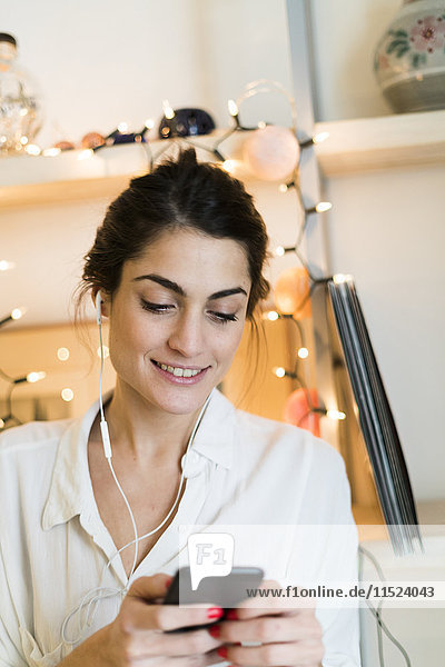 Porträt einer lächelnden Frau beim Musikhören mit Kopfhörer und Smartphone