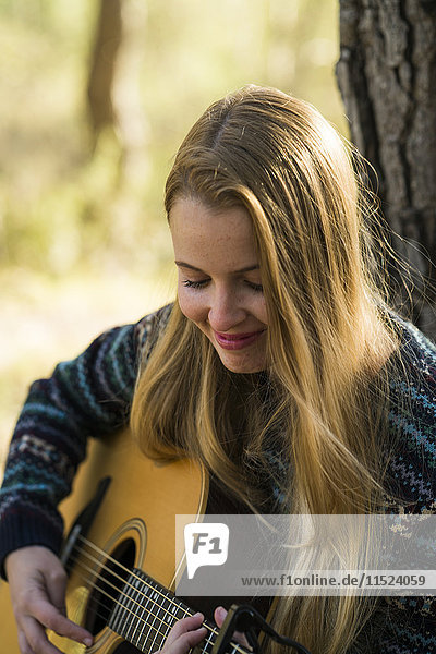 Lächelnde junge Frau spielt Gitarre in der Natur