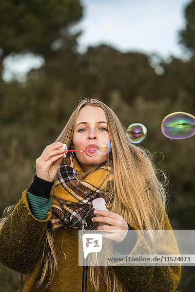 Portrait of young woman blowing soap bubbles in nature