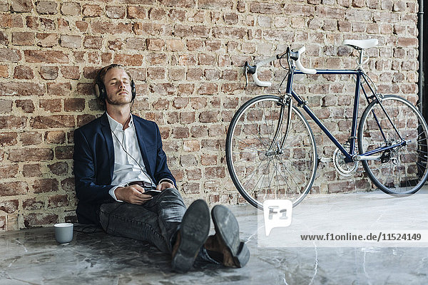 Relaxed man with headphones leaning against brick wall