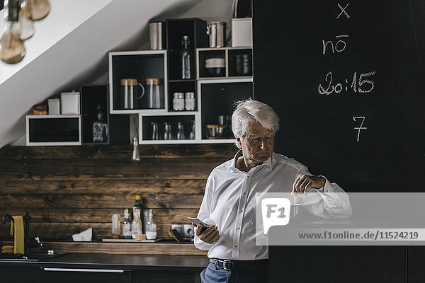 Senior Geschäftsmann mit Smartphone und Tasse Kaffee in der Küche