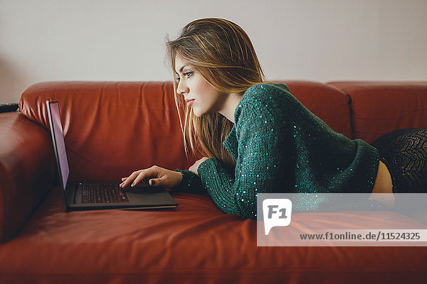 Junge Frau auf der Couch liegend mit Laptop