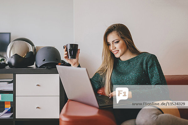 Junge Frau entspannt auf der Couch bei einer Tasse Kaffee mit Laptop
