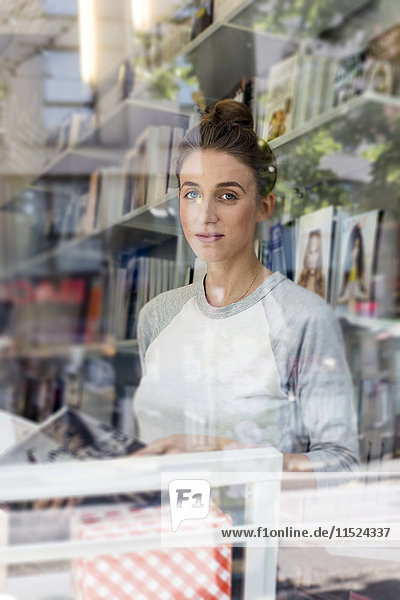 Junge Frau in einer Buchhandlung mit Blick durchs Fenster