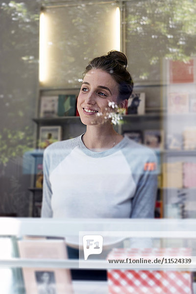 Porträt einer lächelnden jungen Frau in einer Buchhandlung mit Blick durchs Fenster