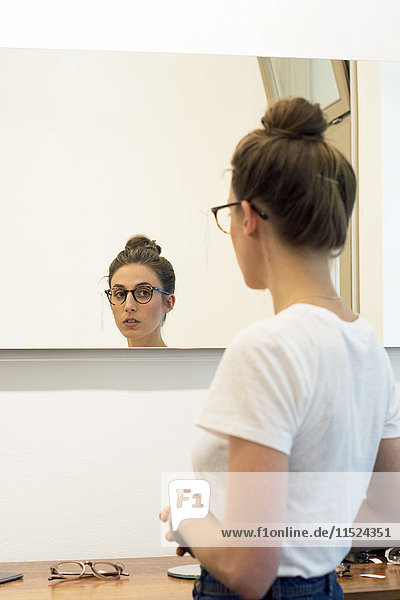 Junge Frau testet Brillenfassungen in einem Optikergeschäft