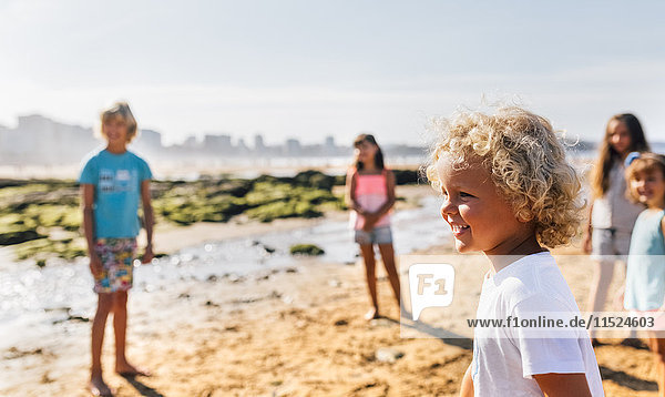 Happy little boy on the beach with other children standing in the background