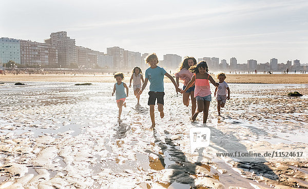 Group of six children running together on the beach