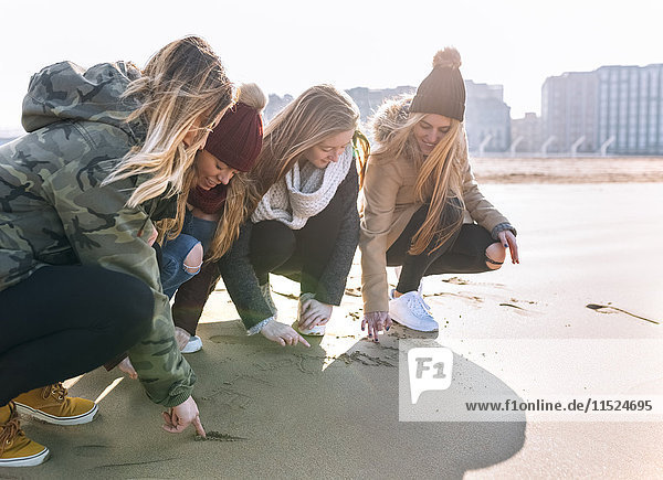Vier Freunde beim Zeichnen im Sand am Strand
