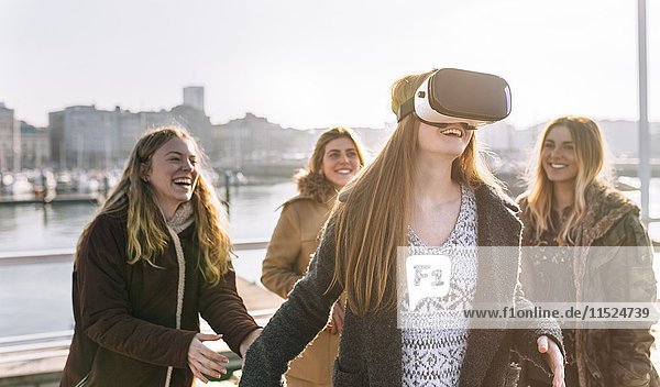 Teenager-Mädchen  das eine VR-Brille trägt  während ihre Freunde sie beobachten.