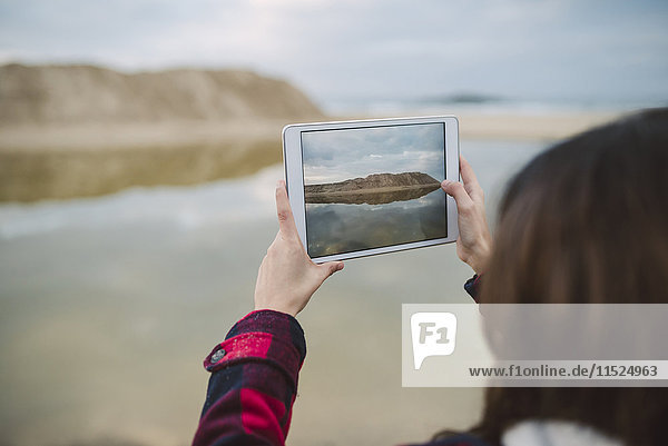 Junge Frau beim Fotografieren mit Tablette am Strand