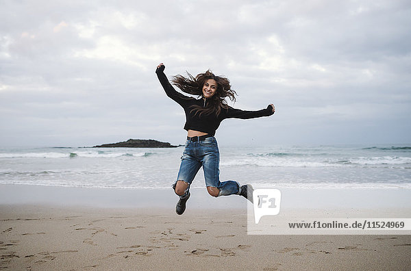 Glückliche Frau  die am Strand in die Luft springt.