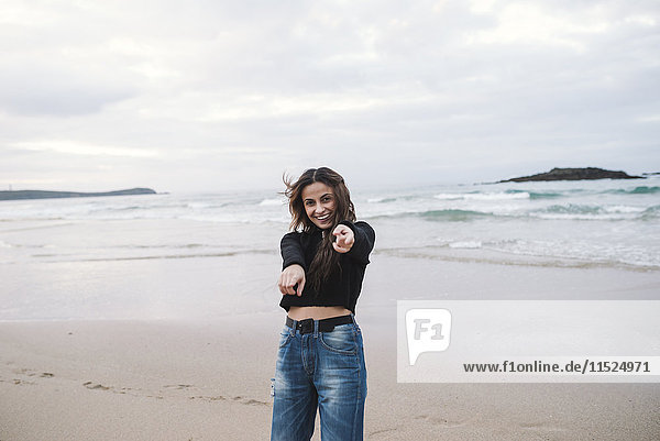 Porträt einer glücklichen jungen Frau am Strand  die auf den Betrachter zeigt.