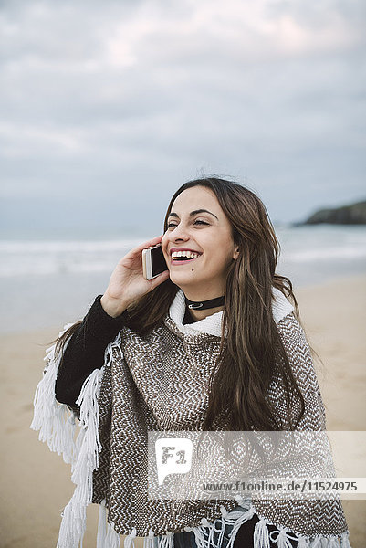 Porträt einer glücklichen jungen Frau am Telefon am Strand