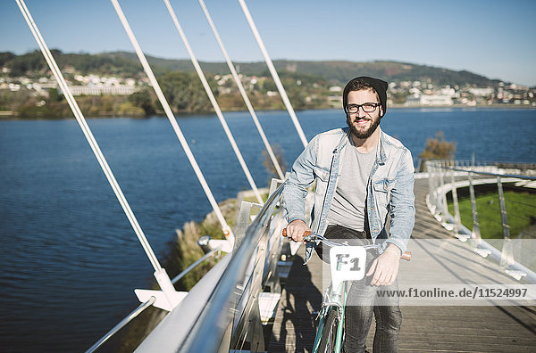 Smiling young man with his fixie bike on a bridge