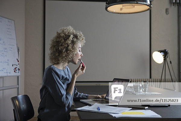 Frau im Büro beim Schminken mit Laptop-Monitor als Spiegel