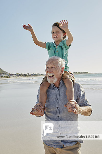 Portrait of senior man with happy grandson on his shoulders on the beach
