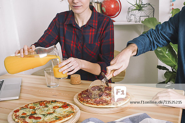 Junges Paar isst Pizza und trinkt Saft zum Mittagessen  Laptop steht auf dem Tisch