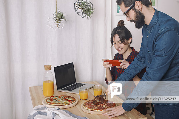 Junges Paar beim Pizzaessen und Safttrinken zum Mittagessen  Frau beim Fotografieren mit Smartphone