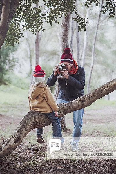 Vater beim Fotografieren seines Sohnes auf einem Baumstamm im Wald