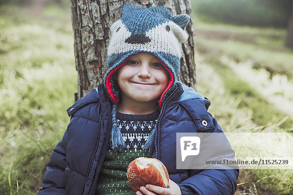 Porträt eines grinsenden Jungen beim Essen eines Berliner im Wald