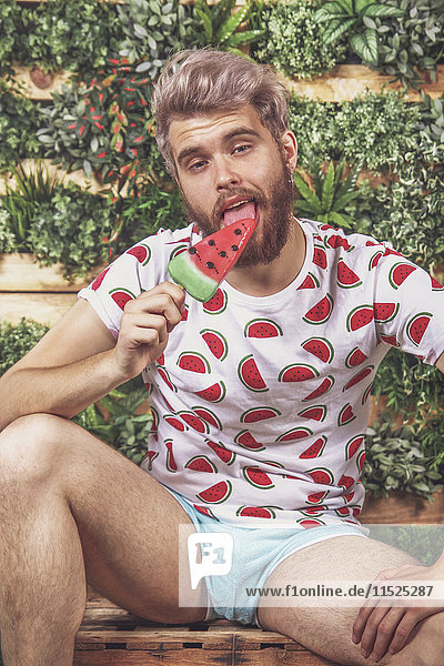 Portrait of young man eating watermelon ice lolly on terrace in front of vertical garden