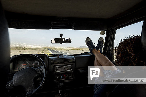 Frau im Auto sitzend mit den Füßen nach oben auf dem Armaturenbrett