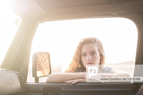 Porträt einer jungen Frau  die sich auf das Autofenster lehnt und nach innen schaut.