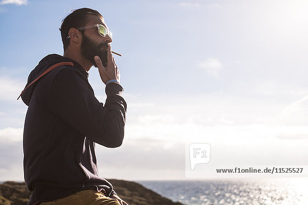 Portrait eines Mannes  der Zigarillo raucht  während er auf das Meer schaut.