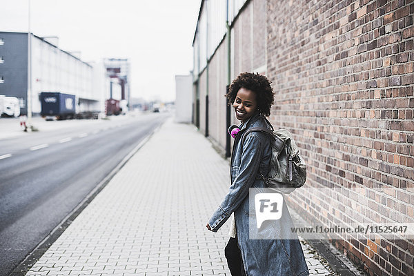 Smiling young woman with headphones and backpack on pavement