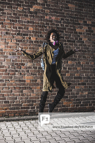 Happy young woman jumping in the air in front of brick wall