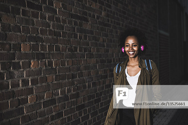 Smiling young woman in front of brick wall listening music with headphones