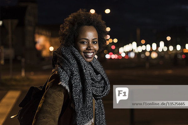Porträt einer lächelnden jungen Frau am Straßenrand bei Nacht