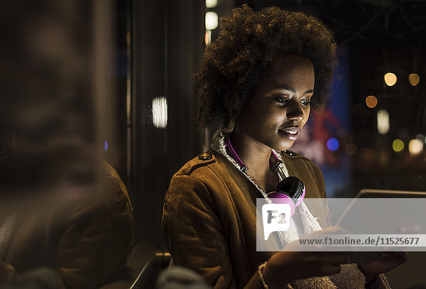 Junge Frau mit Kopfhörer usinf Tablette beim Warten an der Straßenbahnhaltestelle