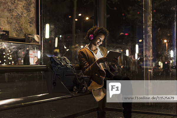 Young woman with headphones and tablet waiting at the tram stop