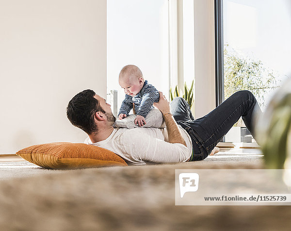 Father playing with baby son  lying on carpet