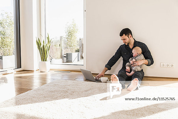 Father with baby son using laptop sitting on floor