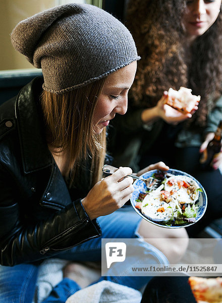 Junge Frau mit Hut  die mit ihren Freunden Salat isst.